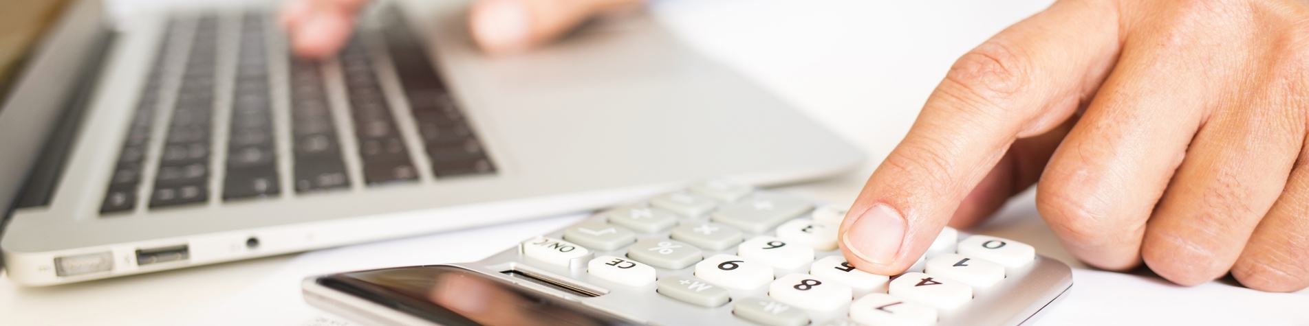 Mand gennemgår regnskab siddende ved bærbar og med lommeregner