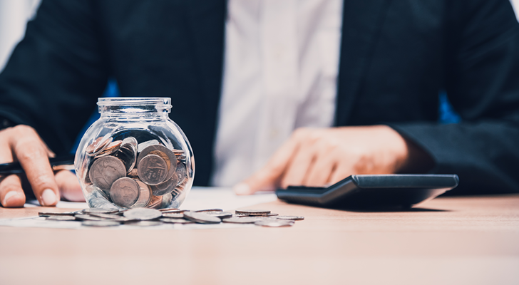 Person tæller penge op med lommeregner og smider mønter i glas