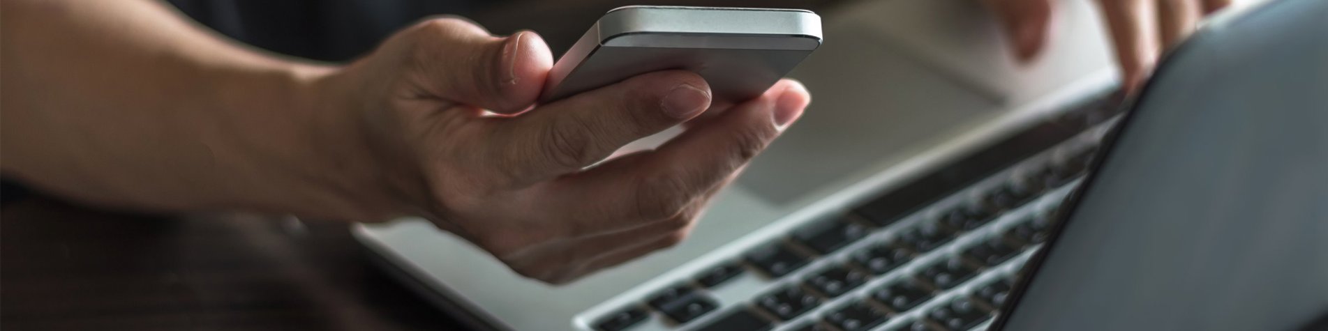 Mand sidder ved bærbar med telefon i hånden