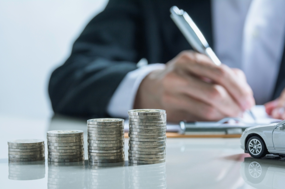 Person skriver kørselsgodtgørelse med stakke af mønter og en lille bil foran sig