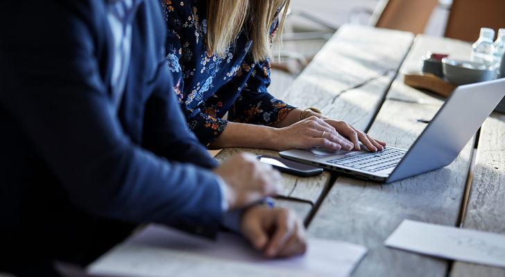 Møde mellem to personer, hvor den ene sidder ved bærbar og den anden med papirer